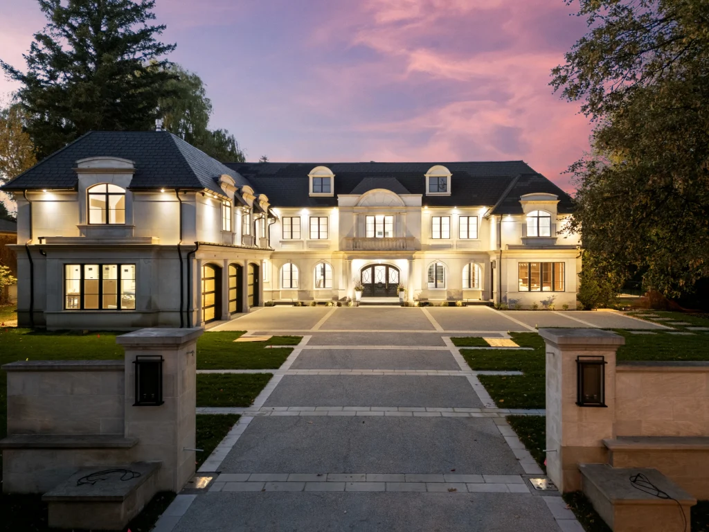 A large stone-clad home at twilight, warm interior light against a pink evening sky